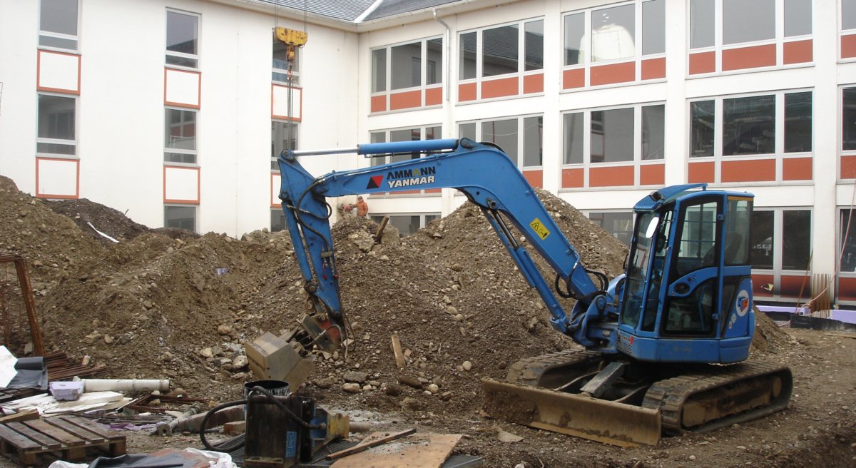 Ein weiterer Meilenstein in der Entwicklung des Gymnasiums Marktoberdorf war die energetische Sanierung der gesamten Schule und die bauliche Erweiterung um einen modernen Verwaltungstrakt im Osten des Schulgeländes in den Jahren 2011-2014. Dabei wurde in der Abbruchphase zu Beginn monatelang schweres Gerät verwendet wie hier der Bagger im Atrium, der über einen riesigen Baukran ins Innere der Schule gehoben wurde. Drei Jahre lang wurde die Schule bei laufendem Betrieb saniert und erweitert, was einen Kraftakt für die gesamte Schulfamilie darstellte, den alle Lehrkräfte, Schüler und Eltern mit großer Disziplin und dem nötigen Langmut bravourös gemeistert haben. Blickt man heute auf das Schulgebäude, dann kann man nur sagen: Es hat sich mehr als gelohnt!