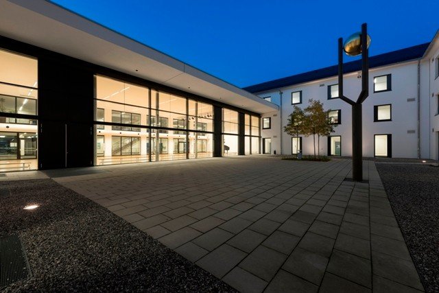 Die Zeitkugel im Atrium des Gymnasiums umschließt die Idee, dass die Klassen, dass die Kurse und Fachschaften in miniaturisierter Form alltagsrelevante Dinge oder - in Textdarlegung - die Wertsetzungen, Vorstellungen, Trends, aktuelle Erscheinungen etc., die sich in den Köpfen als wichtig und zeitmächtig abgebildet haben, in die Zeitkugel einlagern, wo sich dann dieser Querschnitt des jetzigen Lebens in eine konkrete Botschaft in das Jahr 2100 verwandelt, in dem Sinne: So war es bei uns, so haben wir gedacht und unser Leben in die Zukunft hinein gedanklich bzw. visionär fortgesetzt. Eine stumme Botschaft also vom Festland Marktoberdorf 1999 aus an ein fernes und uns unbekanntes Ufer. In 100 Jahren also soll diese &quot;Zeitkugel&quot; geöffnet werden - bis dahin steht sie als Skulptur, als eine Stimmgabel für das 3. Jahrtausend im Schutzraum des Atriums der Schule. Für die Zuarbeit und Organisation der Sammlung sei Herrn Peter Heydenreuter besonders jubilar und sogar säkular gedankt. Er hat sich mit Herzblut investiert und hat bewiesen, dass er die Kraft und in jeder Hinsicht die nötige Spannweite zum Abheben hat - über alle Wolken, d. h. über alle realen Hürden hinweg.