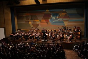 Wenn ein üppig besetztes Sinfonieorchester durch die kleine Tür des eisernen Vorhanges auftritt, dann hält der Auftrittsbeifall kaum lange genug durch. Und wenn es die Vorbühne beinahe überfüllt, dann muss der Dirigent (Stefan Dollansky) schon heraufhüpfen, um an sein Pult zu gelangen.