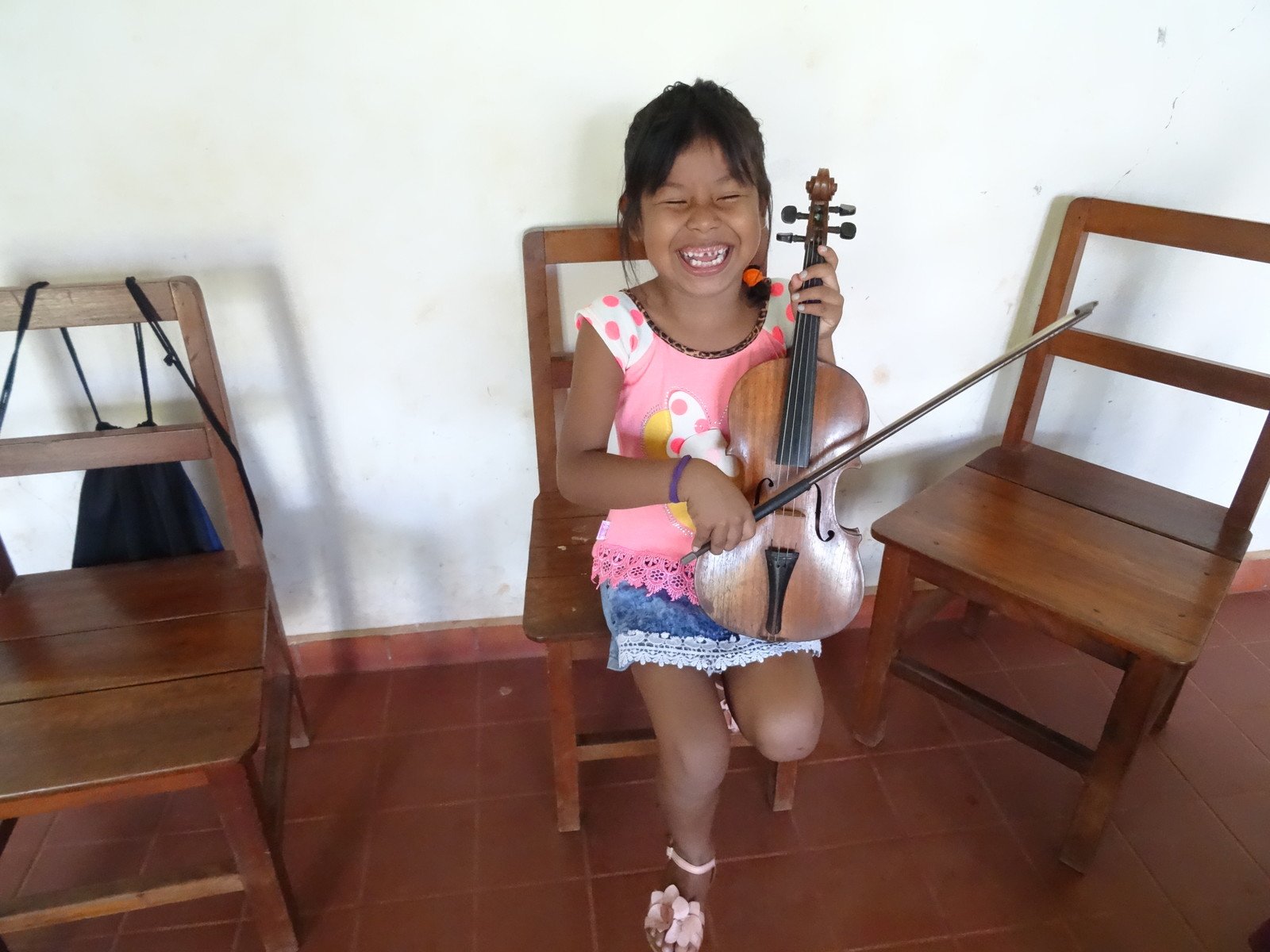 Weil die Geige zu groß ist, versucht die kleine Schülerin das Instrument wie ein Cello zu spielen.